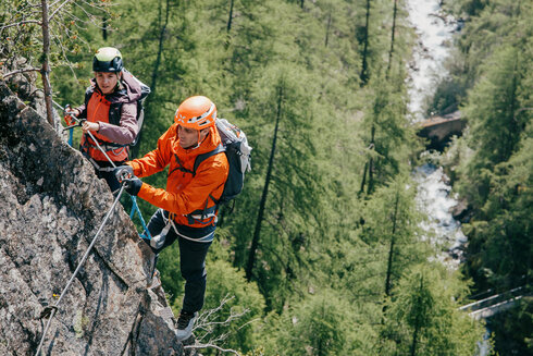 Zwei Erwachsene begehen einen Klettersteig. In der Tiefe kann man die Ötztaler Ache erkennen