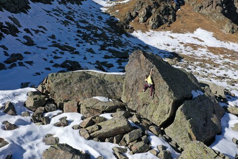 Ein Mann löst ein Boulderproblem an einem Felsbrocken. 