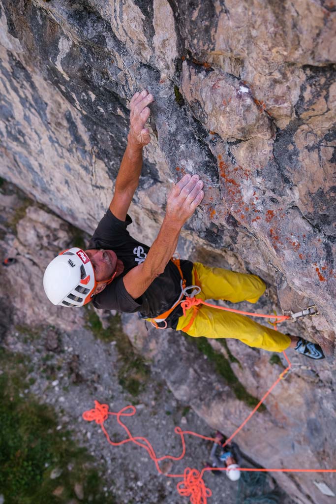 Das bild zeigt einen Kletterer mit gelber Hose auf einer grauen Felswand.