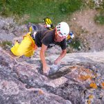 Das bild zeigt einen Kletterer mit gelber Hose auf einer grauen Felswand.